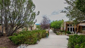 A pathway leading to a building with a covered entrance, surrounded by greenery and trees.