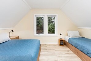 A small, well-lit room with two beds, a nightstand, a radio, and a window with a view of trees.