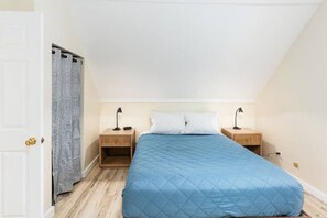 Un dormitorio con una cama, dos mesitas de noche, una mesilla, una puerta y una cortina.