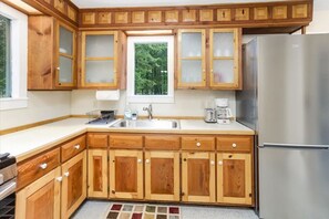 Una cocina con armarios de madera, un refrigerador de acero inoxidable, una ventana con vistas a árboles y una cafetera sobre la encimera.