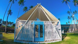 A small, blue, A-frame structure with a door labeled "TABOO Beach Bar" surrounded by palm trees. - Taboo Milagres (São Miguel dos Milagres)