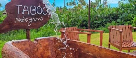 Una bañera de madera con agua brotando, sillas de madera y un letrero que dice "TABOC palaces" bajo un paraguas grande.
