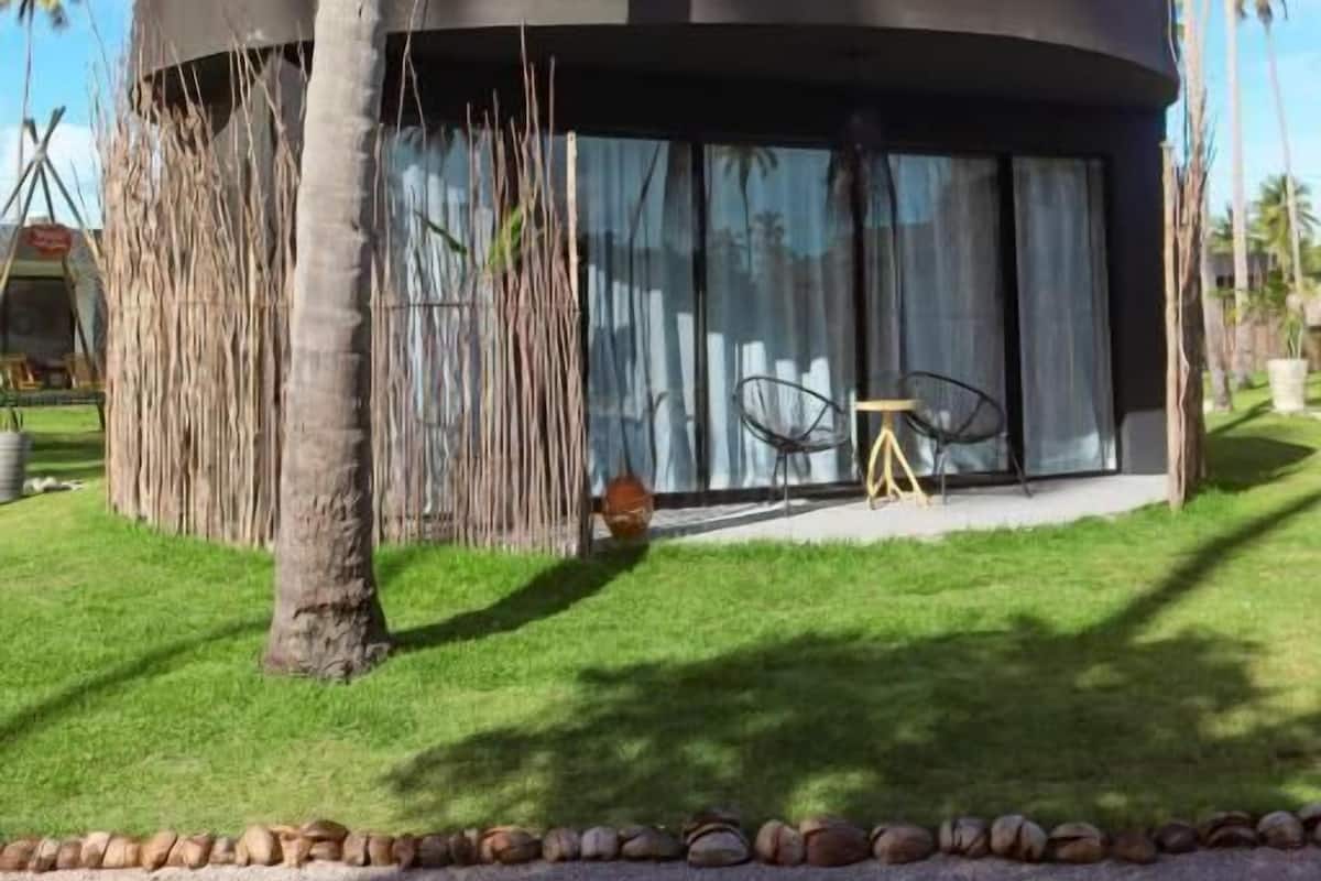 Een modern, rond gebouw met grote ramen, omgeven door palmbomen en een verzorgd gazon.