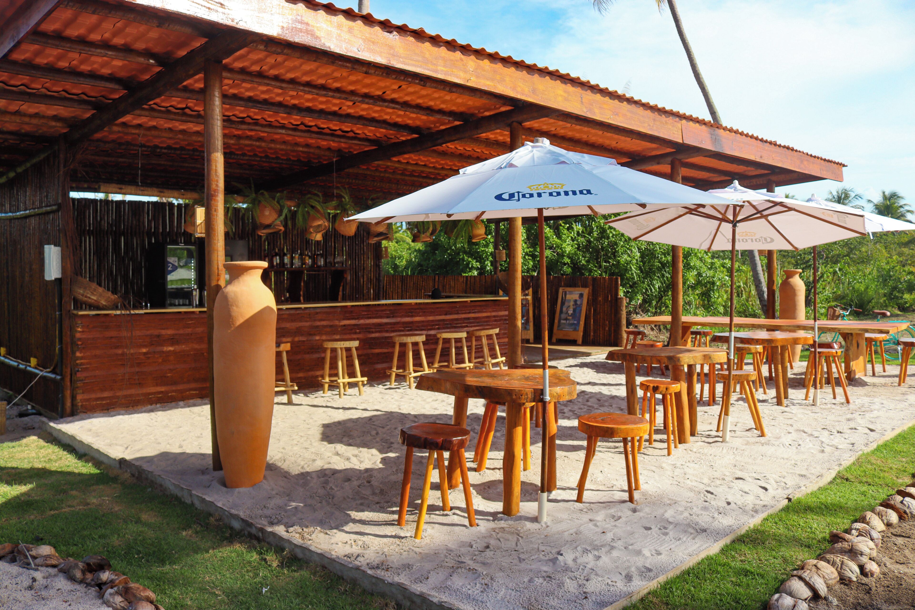 An outdoor seating area with wooden tables and chairs, large umbrellas, and a rustic wooden structure.