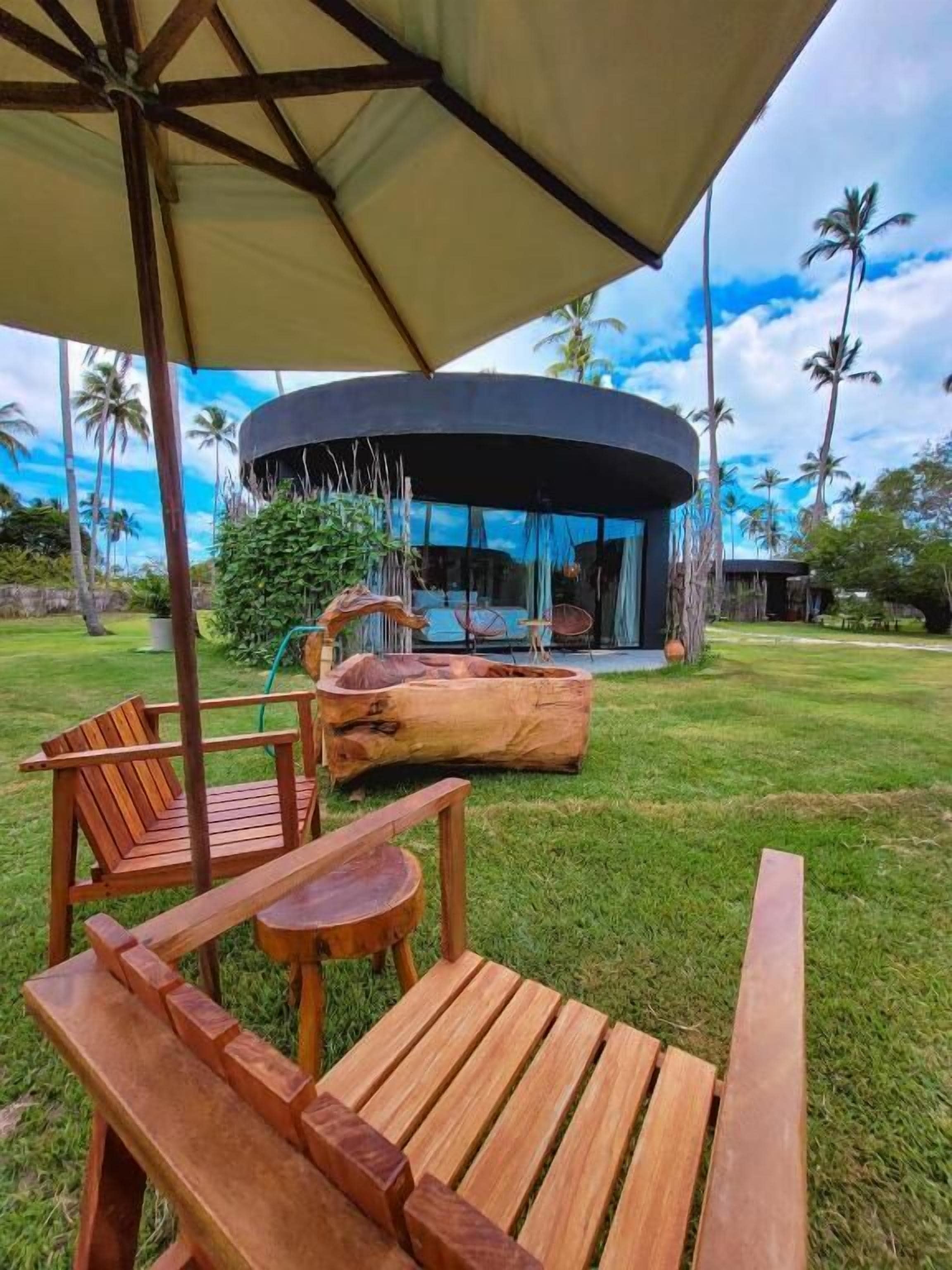 A wooden deck with a round table and chairs, a large umbrella, and a circular building with a glass facade.