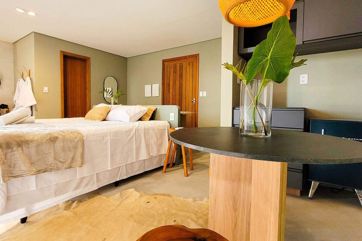 Een moderne slaapkamer met twee bedden, een houten bijzettafeltje, een groot raam en een keukenhoek.