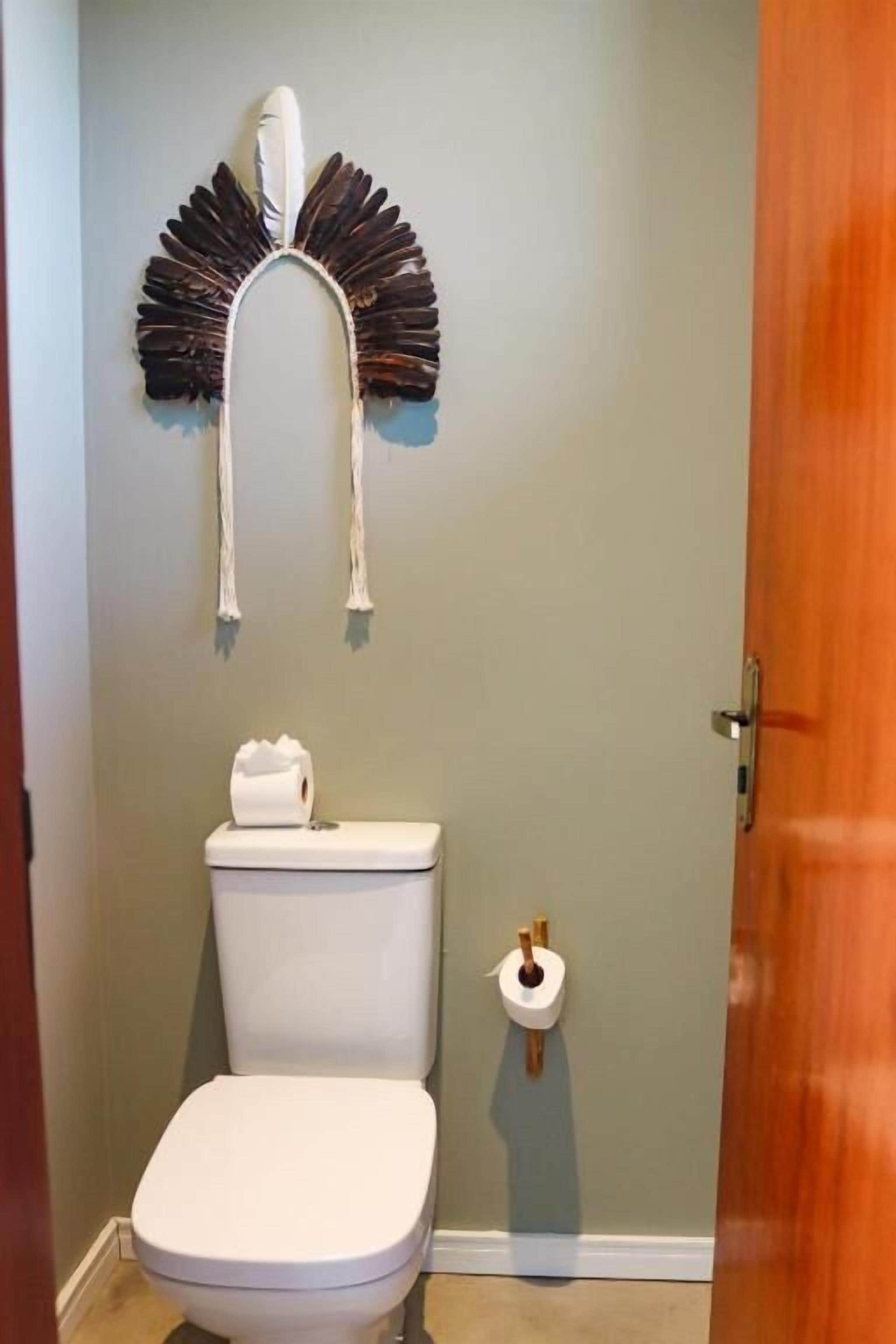 Un baño con inodoro, dispensador de papel higiénico y un adorno en la pared.