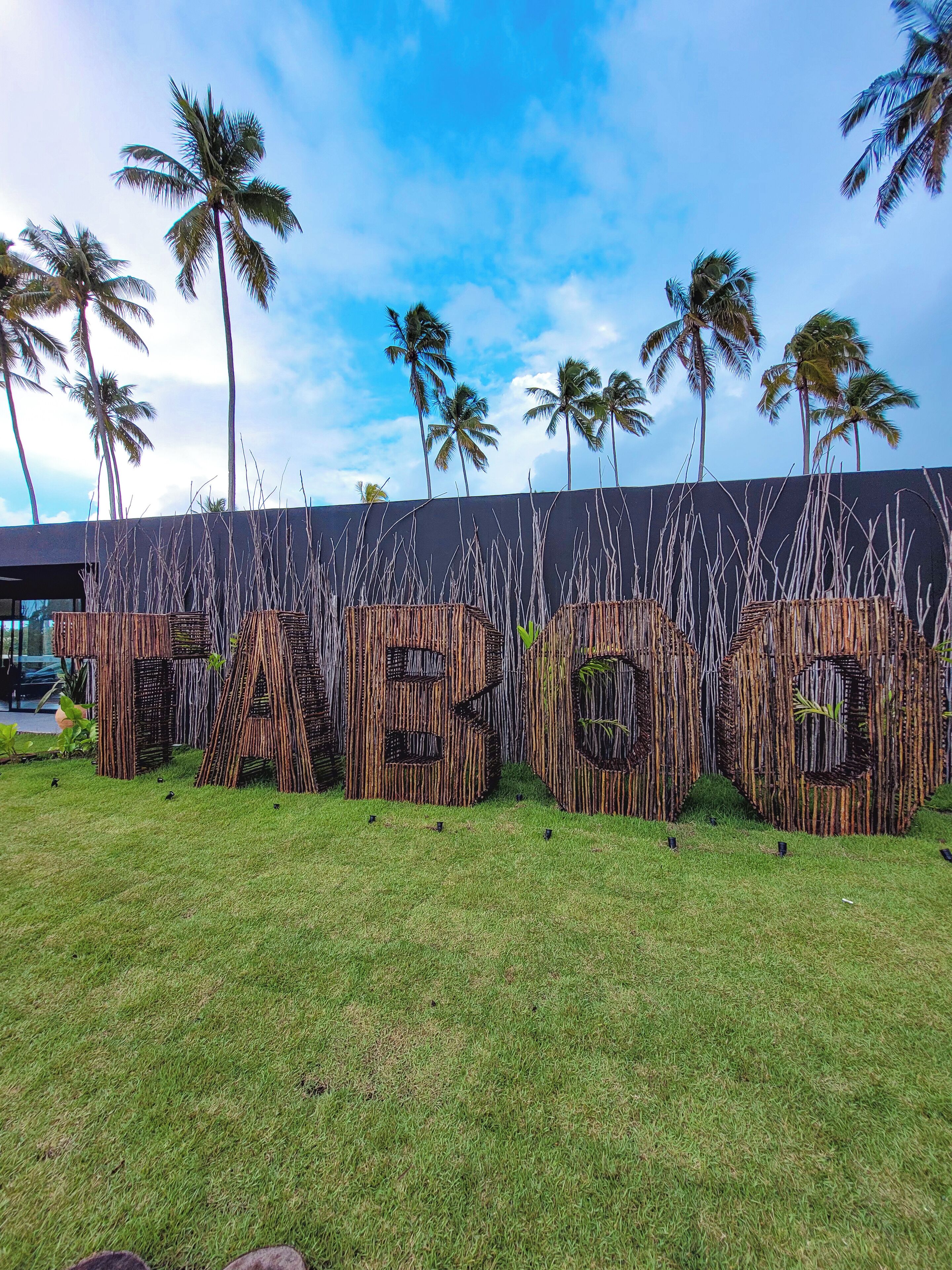 Een tropisch resort met een bamboestructuur waarop 'TIGO' staat en palmbomen op de achtergrond.