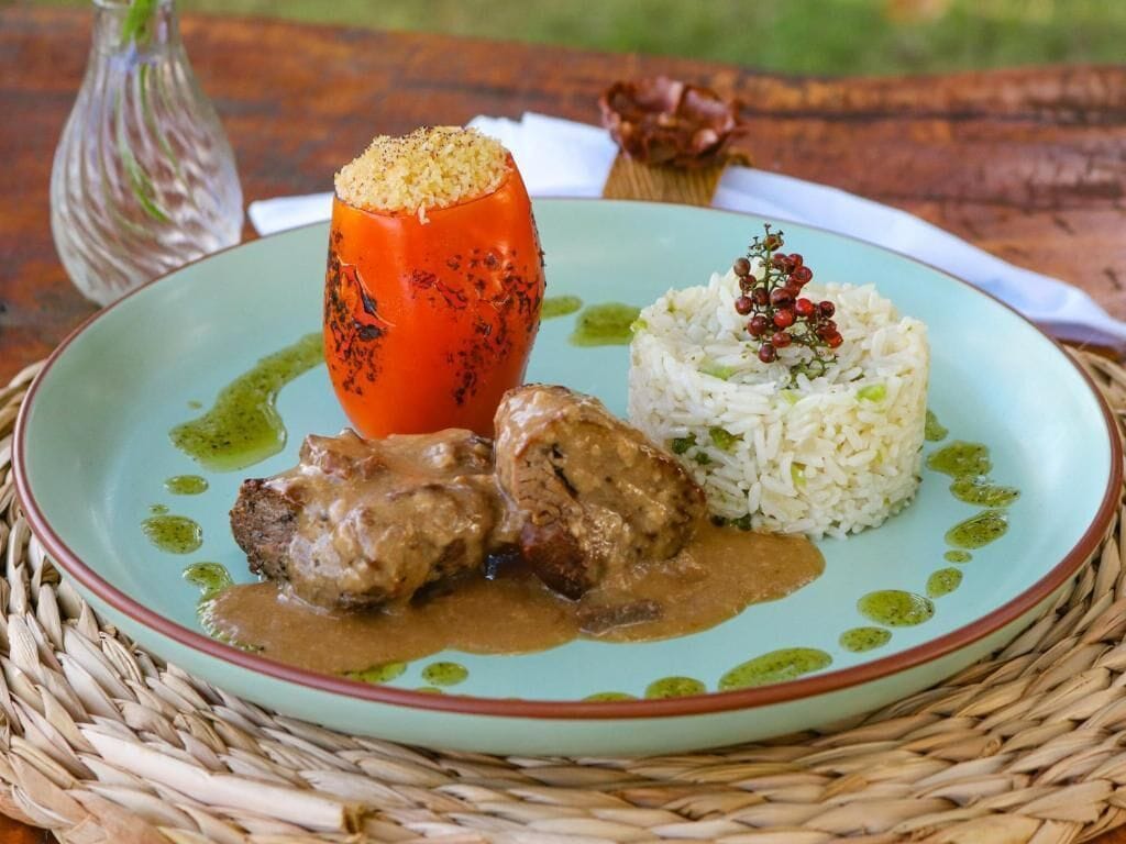 Un plato con tomate relleno, arroz y carne con salsa.