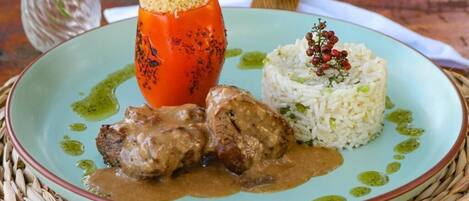 A plate with a stuffed tomato, rice, and meat with gravy.
