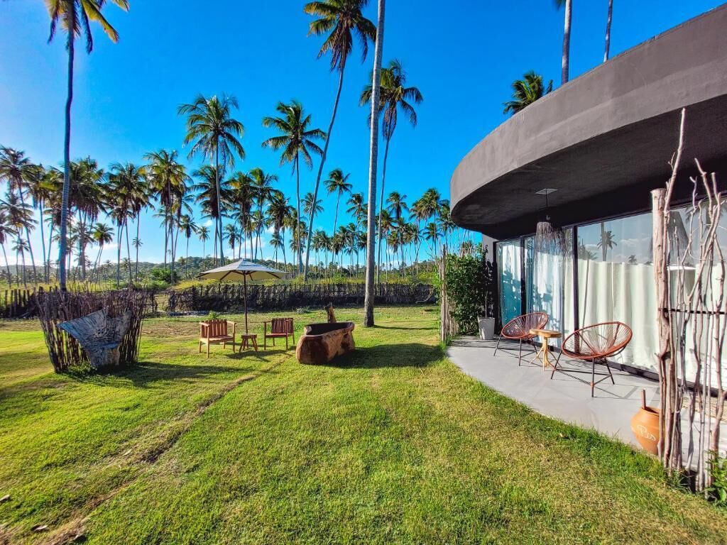 A modern building with a curved exterior, a patio area with outdoor furniture, and a view of palm trees.