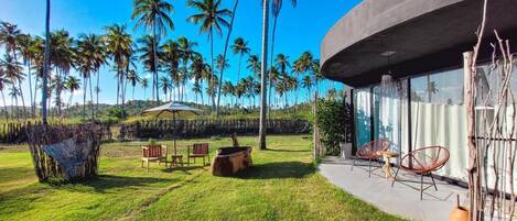 A modern building with a curved exterior, a patio area with outdoor furniture, and a view of palm trees.