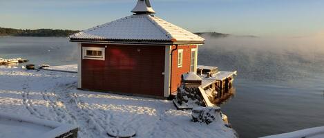 Ein kleines rotes Gebäude mit einem mit Schnee bedeckten Dach, gelegen an einem zugefrorenen See.