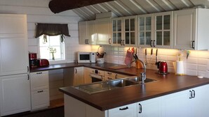 Een keuken met witte kastjes, een magnetron, een spoelbak en een raam met gordijn.
