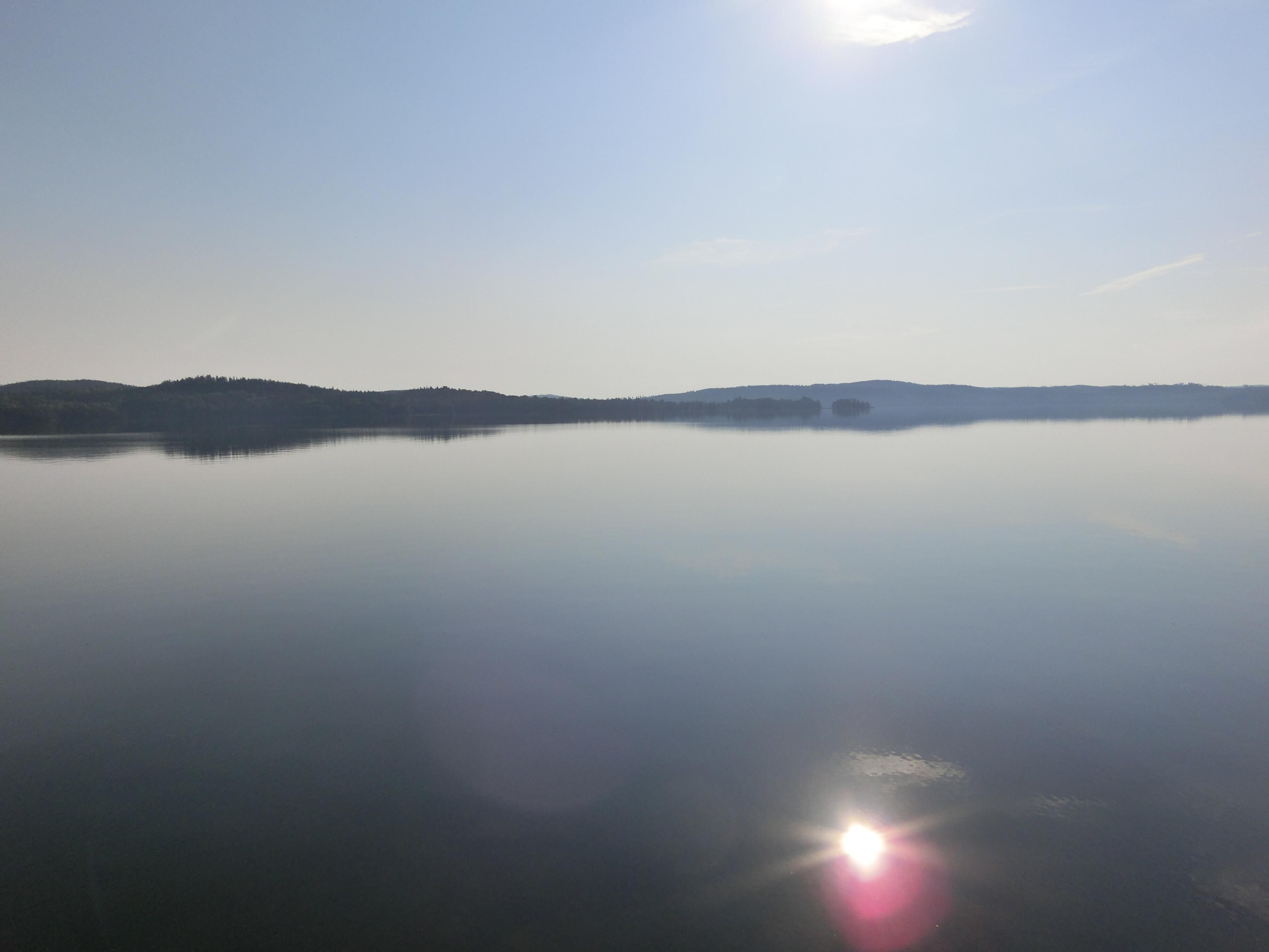 En rolig sø med et klart spejlbillede af himlen og fjerne bakker.