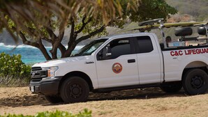 A white C&C Lifeguard vehicle parked near a beach with a surfboard on the back. - Hawaiian Hale  (Hauula)