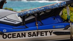 A blue and white Yamaha jet ski with "OCEAN SAFETY" written on the side, set against a coastal backdrop. - Hawaiian Hale  (Hauula)
