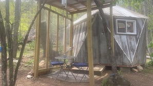Une construction rustique en bois, dotée d’un toit en métal et d’une petite fenêtre, entourée d’arbres.