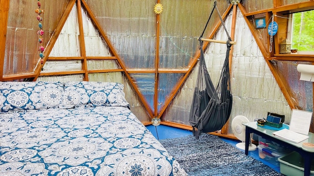 Une tente équipée d’un lit, d’une chaise suspendue et d’une table avec un ventilateur.