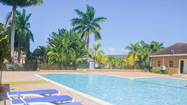 Une piscine entourée de chaises longues bleues, de palmiers et d’un bâtiment doté d’un toit en tuiles.