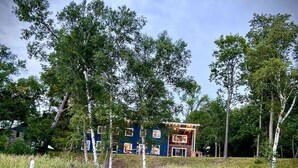 Een gebouw aan de rivier met een steiger die in het water uitsteekt, omringd door hoge bomen en dikke rietkragen.