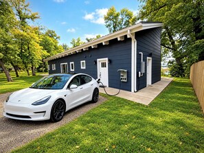 Une voiture blanche est garée devant un bâtiment moderne, à proximité d’une borne de recharge.