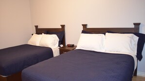Two single beds with wooden headboards, a nightstand with a clock, and a plain wall. - Budget loft with two beds + sofa bed (Le Citadin) (Rouyn-Noranda)