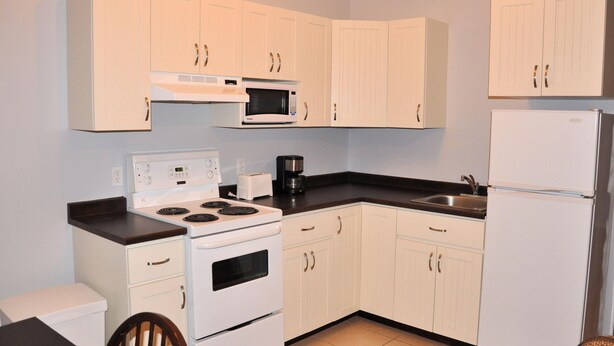 A compact kitchen with white cabinets, a stove, a microwave, a refrigerator, and a coffee maker. - Budget loft with two beds + sofa bed (Le Citadin) (Rouyn-Noranda)