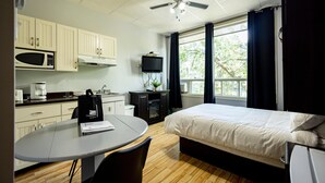A compact hotel room with a bed, a desk, a microwave, a television, and a ceiling fan. - Loft Economique in the heart of Rouyn-Noranda (Le Citadin) (Rouyn-Noranda)
