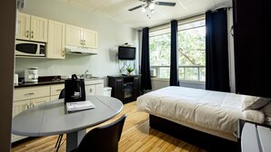 A hotel room with a bed, a desk with a chair, a microwave, a coffee maker, a television, and a window with curtains. - Loft Economique in the heart of Rouyn-Noranda (Le Citadin) (Rouyn-Noranda)
