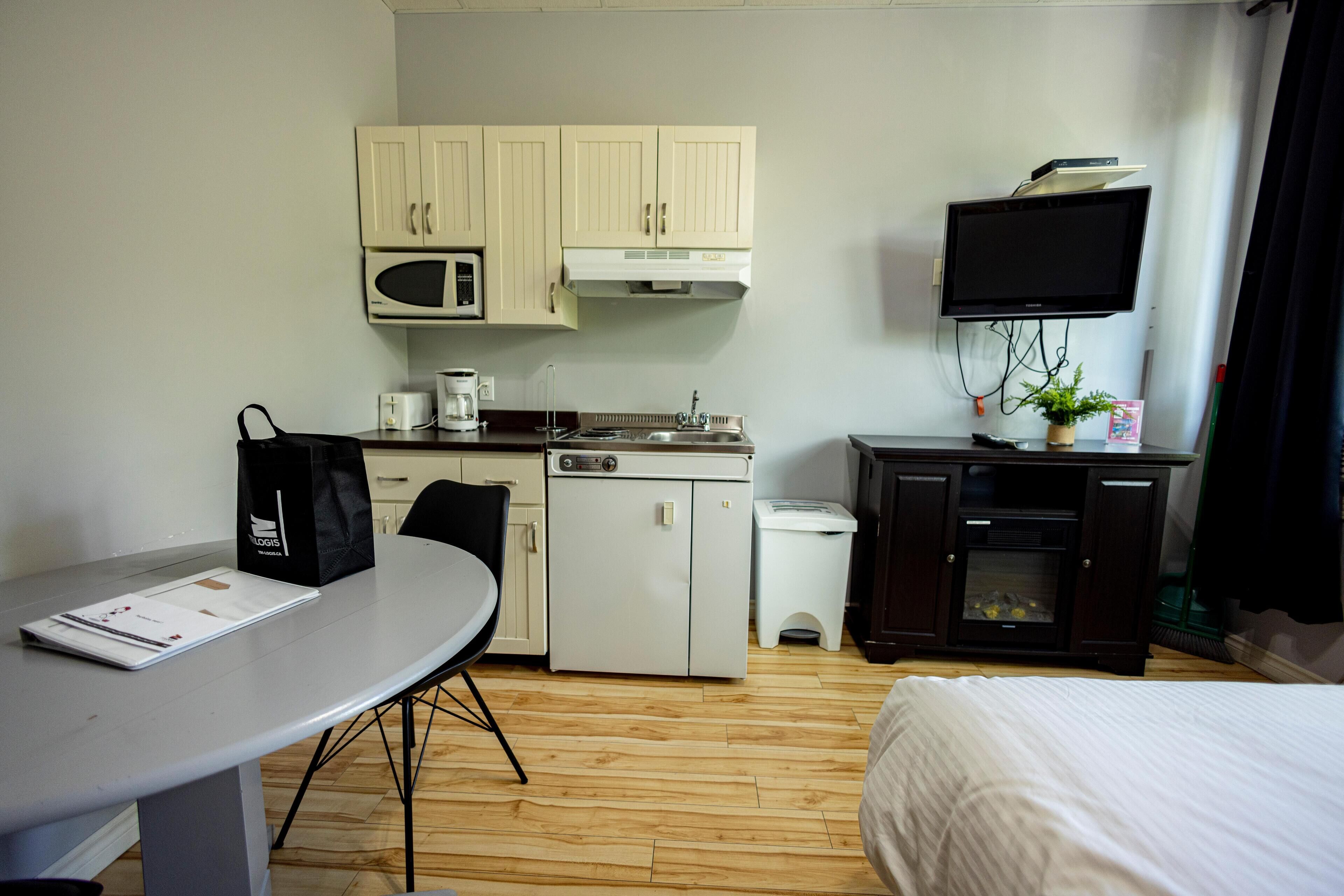 A compact hotel room with a kitchenette, a bed, a dining table, and a TV.