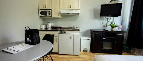 A compact hotel room with a kitchenette, a bed, a dining table, and a TV.