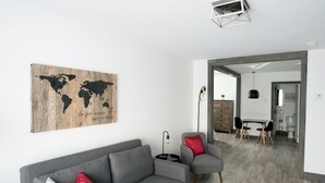 A modern living room with a grey sofa, red and grey cushions, a world map artwork, and a dining area with a table and chairs. - Loft with bed and sofabed in the city centre (Le Court-toit) (Rouyn-Noranda)