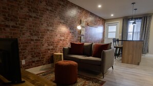 Una sala de estar con pared de ladrillo, un sofá, un reposapiés y un mueble para televisor.