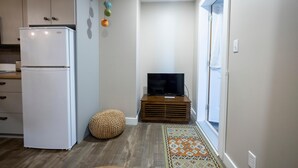 Una cocina compacta con un refrigerador blanco, armarios de madera, un televisor sobre un mueble de madera y una alfombra estampada.
