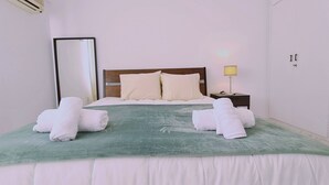Un letto rifatto con cura, con una coperta verde, due cuscini e due asciugamani arrotolati.