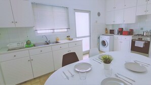 Una cucina moderna con mobili bianchi, una lavatrice integrata e un'area pranzo con tavolo apparecchiato per due.