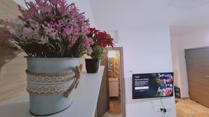 Ein Zimmer mit Fernseher, der einen Anmeldebildschirm zeigt, einer Topfpflanze mit rosa Blüten und einem Holztisch.
