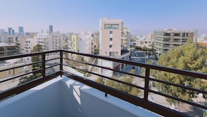 Ein Balkon mit freiem Blick auf eine Stadtansicht, darunter verschiedene Gebäude und ein entfernter Gebirgszug.