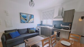 Ein kompakter Wohnbereich mit einer Couch, einem Esstisch und einer Küchenzeile inklusive Waschmaschine und Backofen.