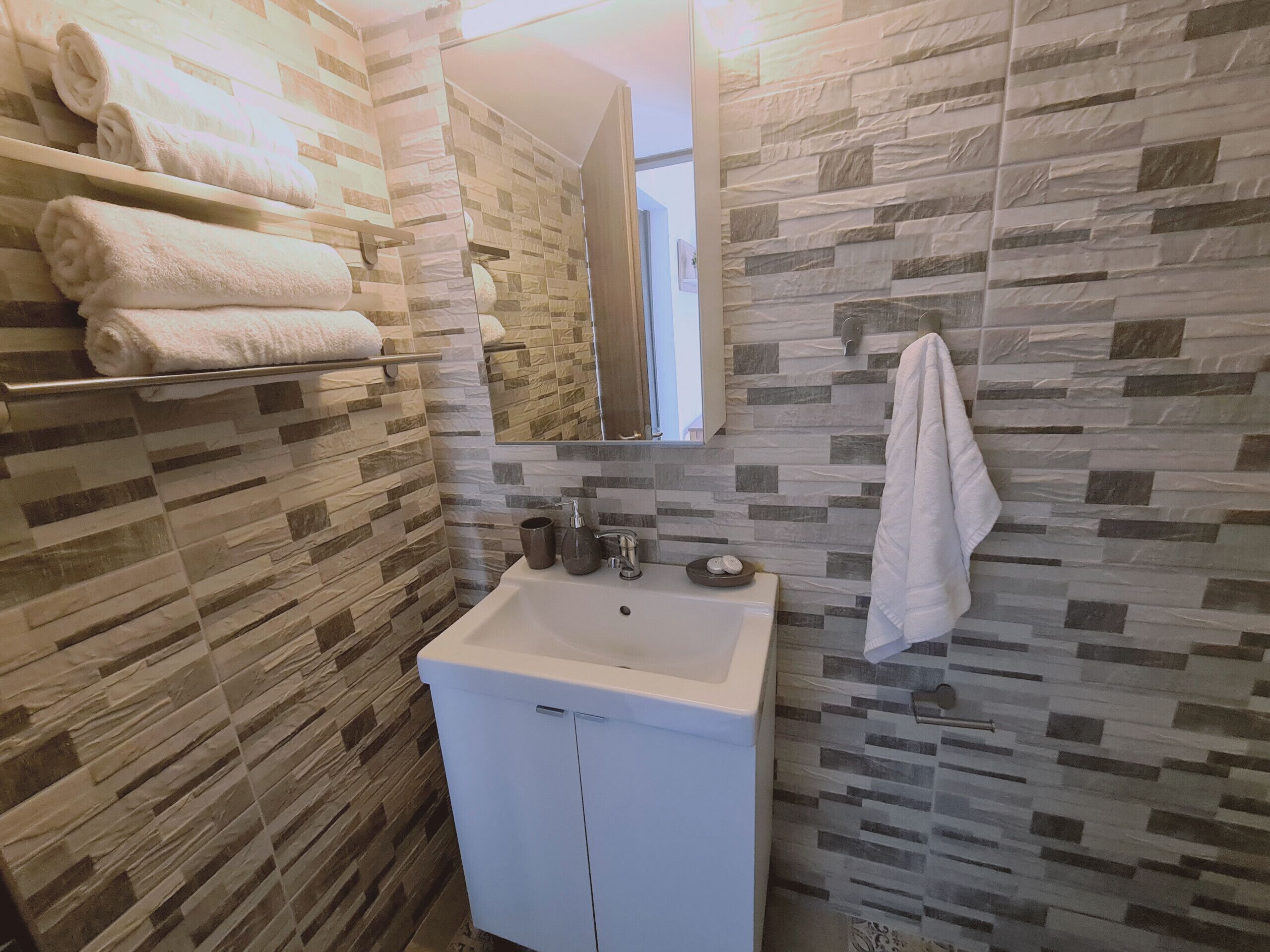 Ein Badezimmer mit einem weißen Waschbecken, einem Spiegel und einem Handtuchhalter mit gefalteten Handtüchern.