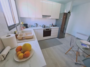 Una cucina moderna con mobili bianchi, un frigorifero in acciaio inossidabile e un tavolo in vetro.