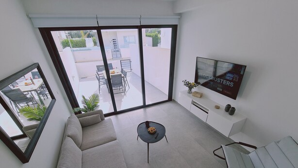 Un salon moderne avec un canapé, une table basse et un téléviseur fixés sur un mur blanc.