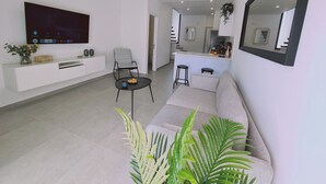 Un salon moderne doté d’un téléviseur à écran plat, d’un canapé, d’une table basse et d’un coin repas avec des tabourets.