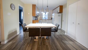 Una cocina moderna con una isla grande, luces colgantes y un comedor con una mesa y sillas blancas.