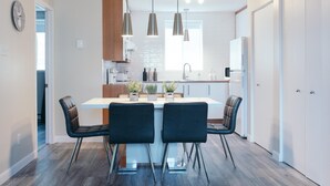 Una cocina moderna con una isla central, luces colgantes y un comedor con cuatro sillas.