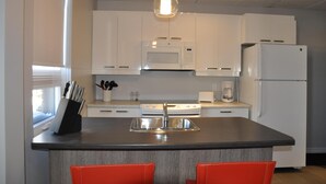A modern kitchen with white cabinets, a microwave, a stove, and a refrigerator. - Suite with closed bedroom and sofa bed on the rue Principale (Le Chic-urbain) (Rouyn-Noranda)