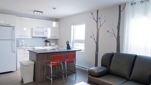 A modern kitchen with white cabinets, a central island with red chairs, a dark leather sofa, and a wall mural. - Suite with closed bedroom and sofa bed on the rue Principale (Le Chic-urbain) (Rouyn-Noranda)
