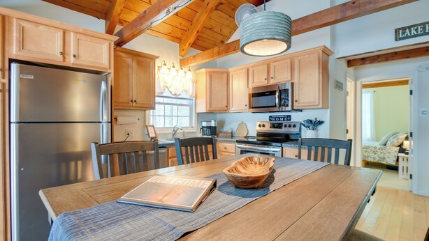 Una cocina con armarios de madera, un refrigerador de acero inoxidable, un microondas y una mesa de comedor con un posavasos y un tazón.