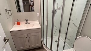 Een moderne badkamer met een douchecabine van glas, een wit toilet en een wastafel met spiegel.